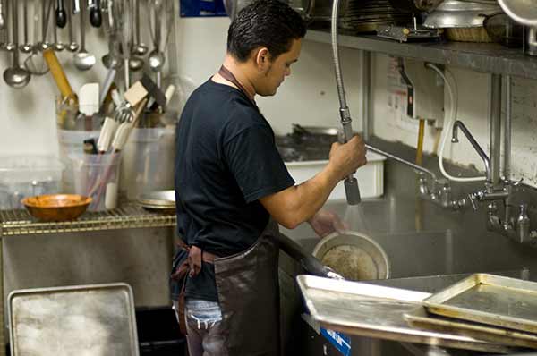 Dishwasher in restaurant with greasy pans